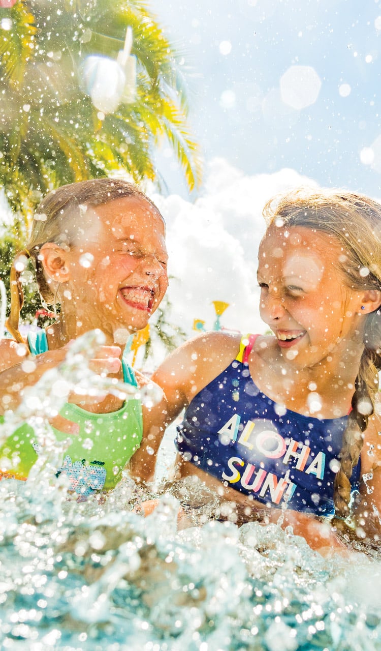 Two young girls laughing and splashing in a pool