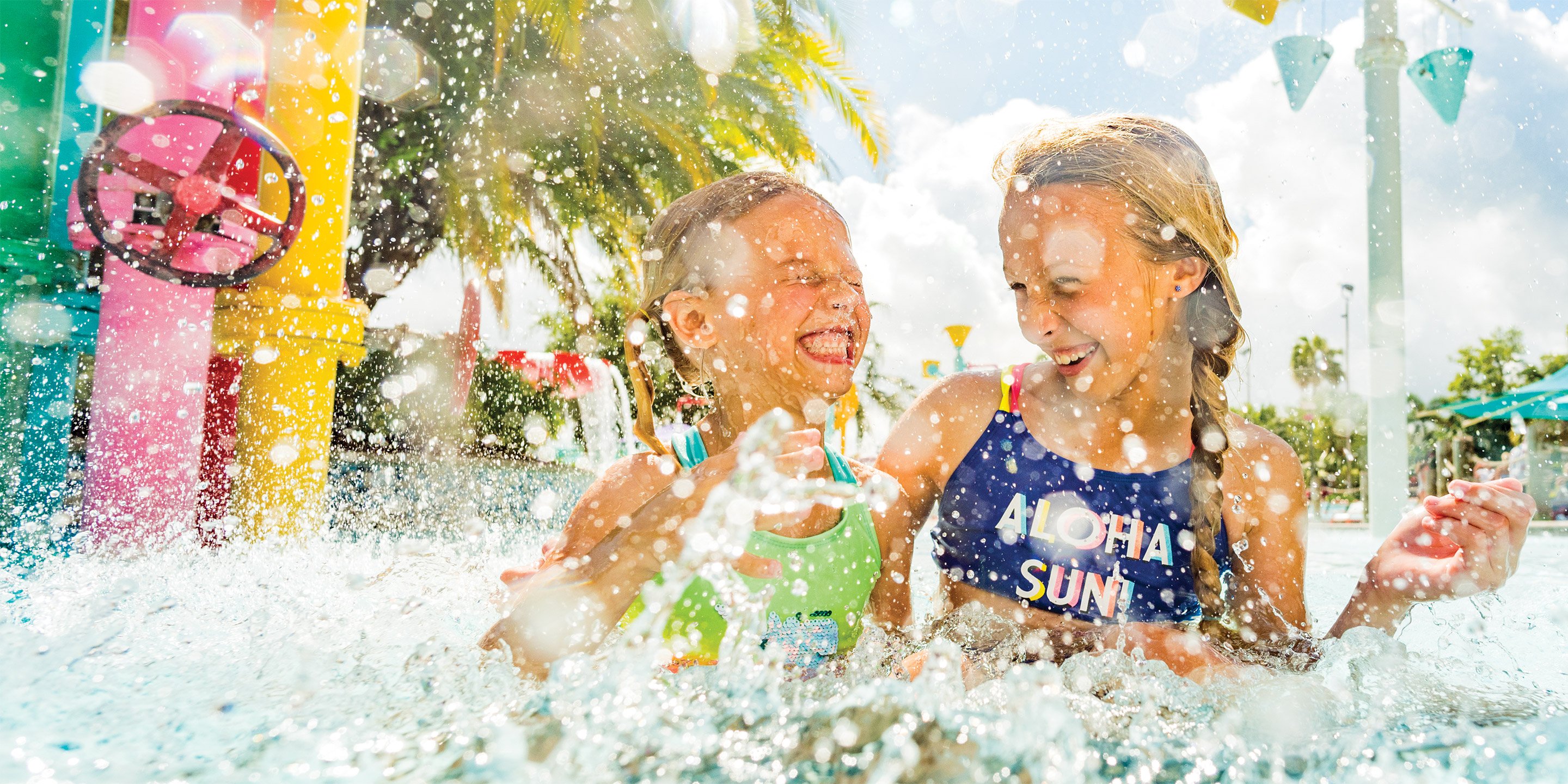 Two young girls laughing and splashing in a pool