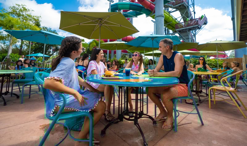 Four people sitting outside at a table with an umbrella