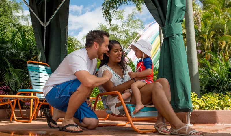 A man and a woman with a baby on a beach chair in a cabana